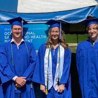 Four graduates in front of the GVSU OSH program banner